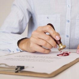 person-using-wax-seal-front-view A person pressing a red wax seal onto a document on a clipboard