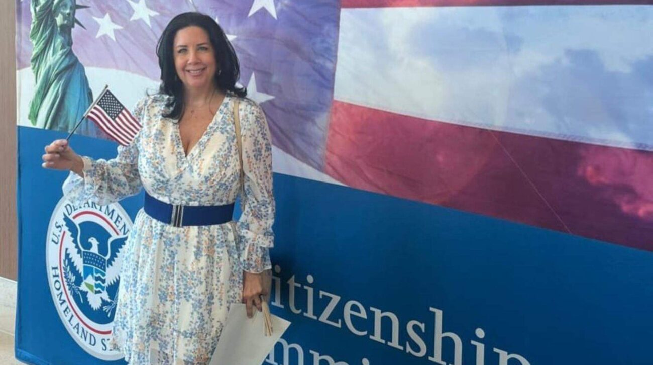 3 Smiling woman in a floral dress holding a small American flag in front of a U.S. Citizenship and Immigration Services backdrop