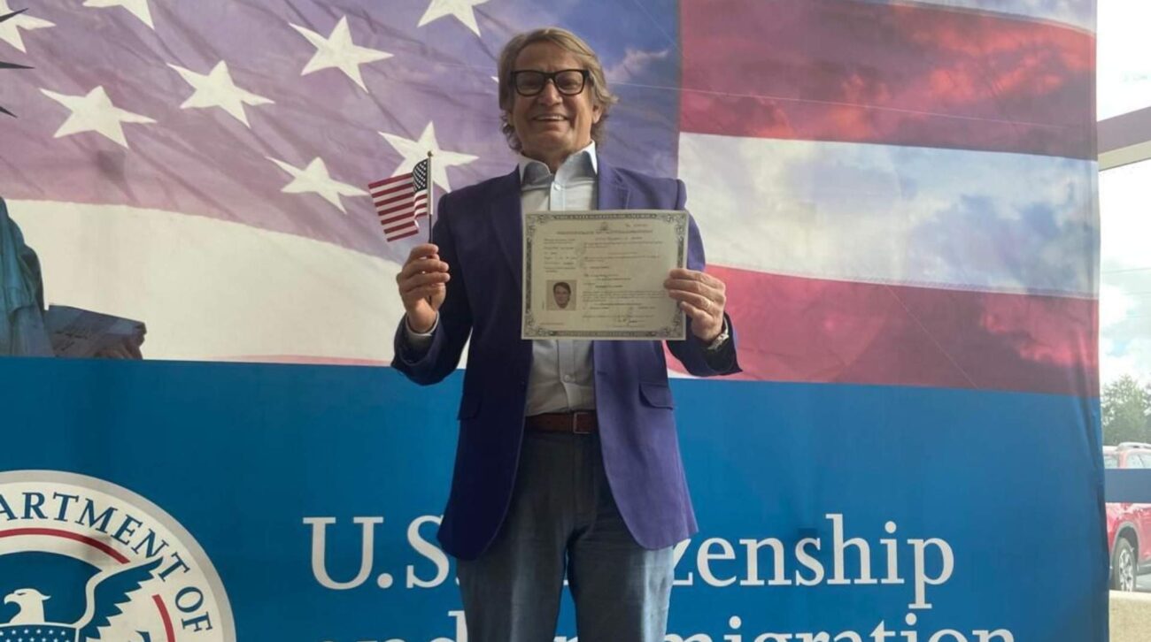 clientes Smiling man in a blue blazer holding a U.S. citizenship certificate and a small American flag