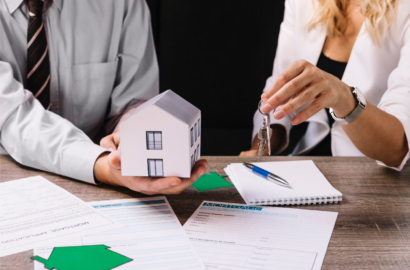 A person handing over house keys to another holding a model house over paperwork