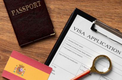 A passport, a visa application form, a Spanish flag, and a magnifying glass on a desk