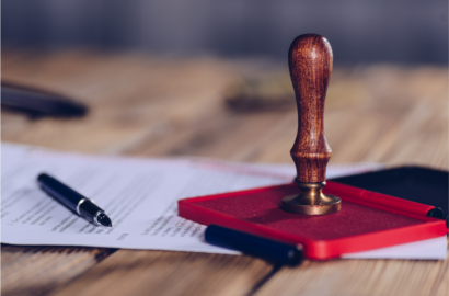 A wooden rubber stamp resting on a red ink pad beside a pen and a document